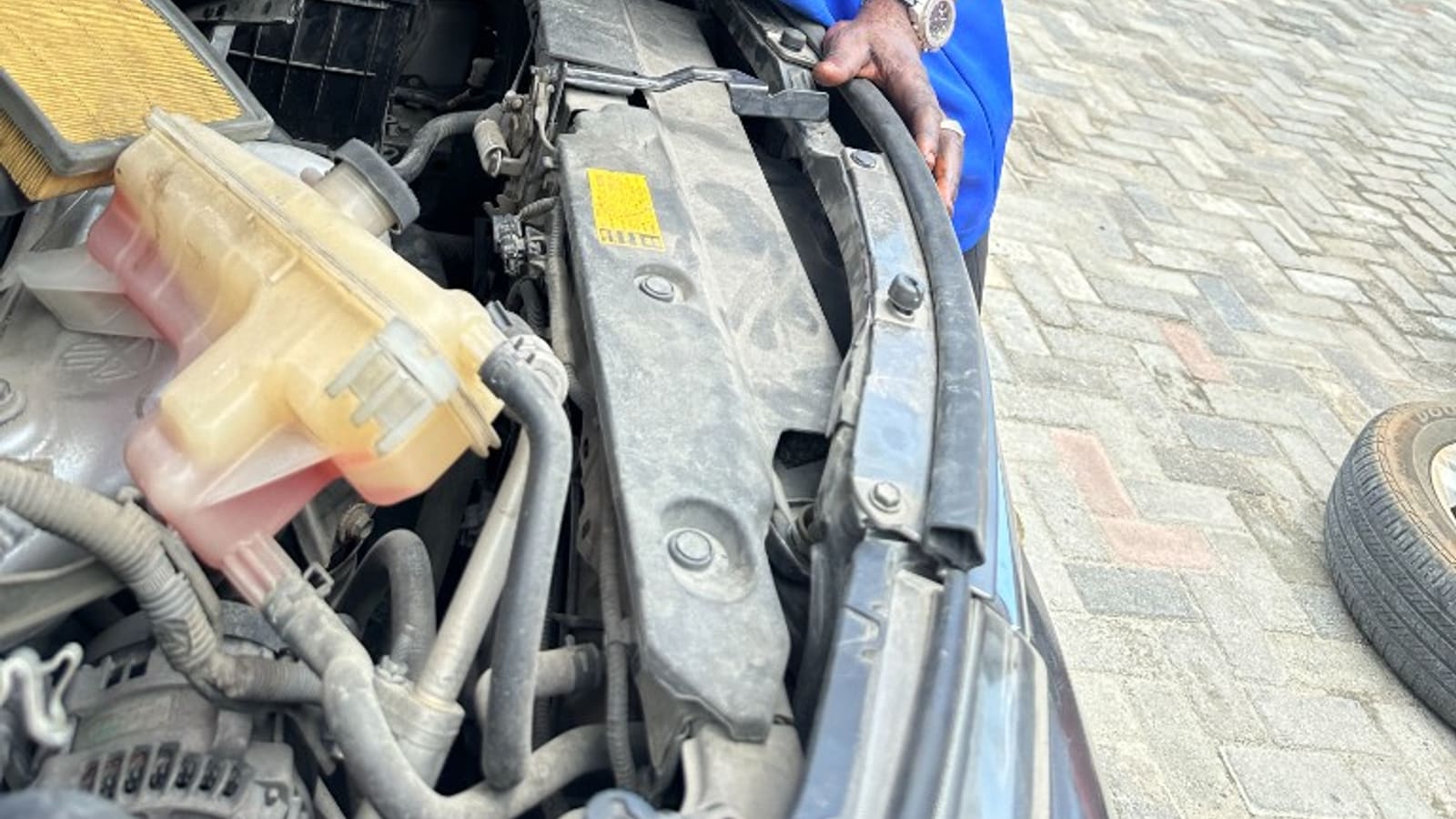 Nigerian automotive AC and electrical specialist working at the engine bay in a Lagos workshop