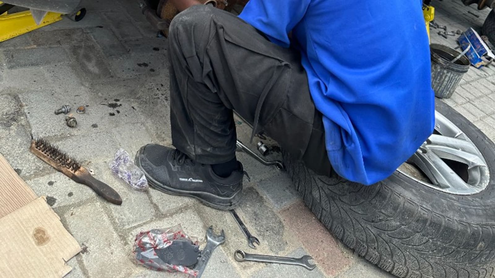 Nigerian mechanic performing brake and undercar inspection on a lifted vehicle